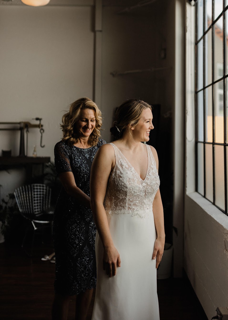 bride looking out the window while mom is helping her with