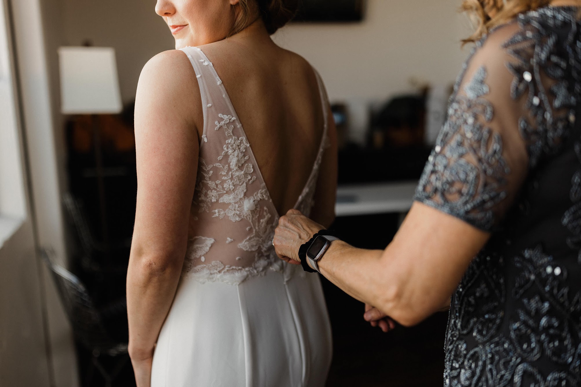 mom helping her daughter zip the back of her wedding dress 