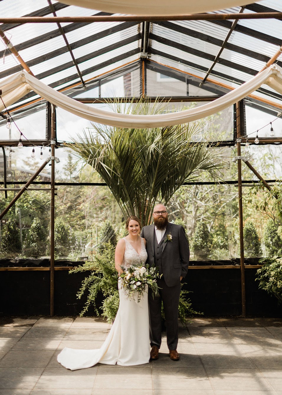 bride and groom standing in the middle of a large greenhouse 