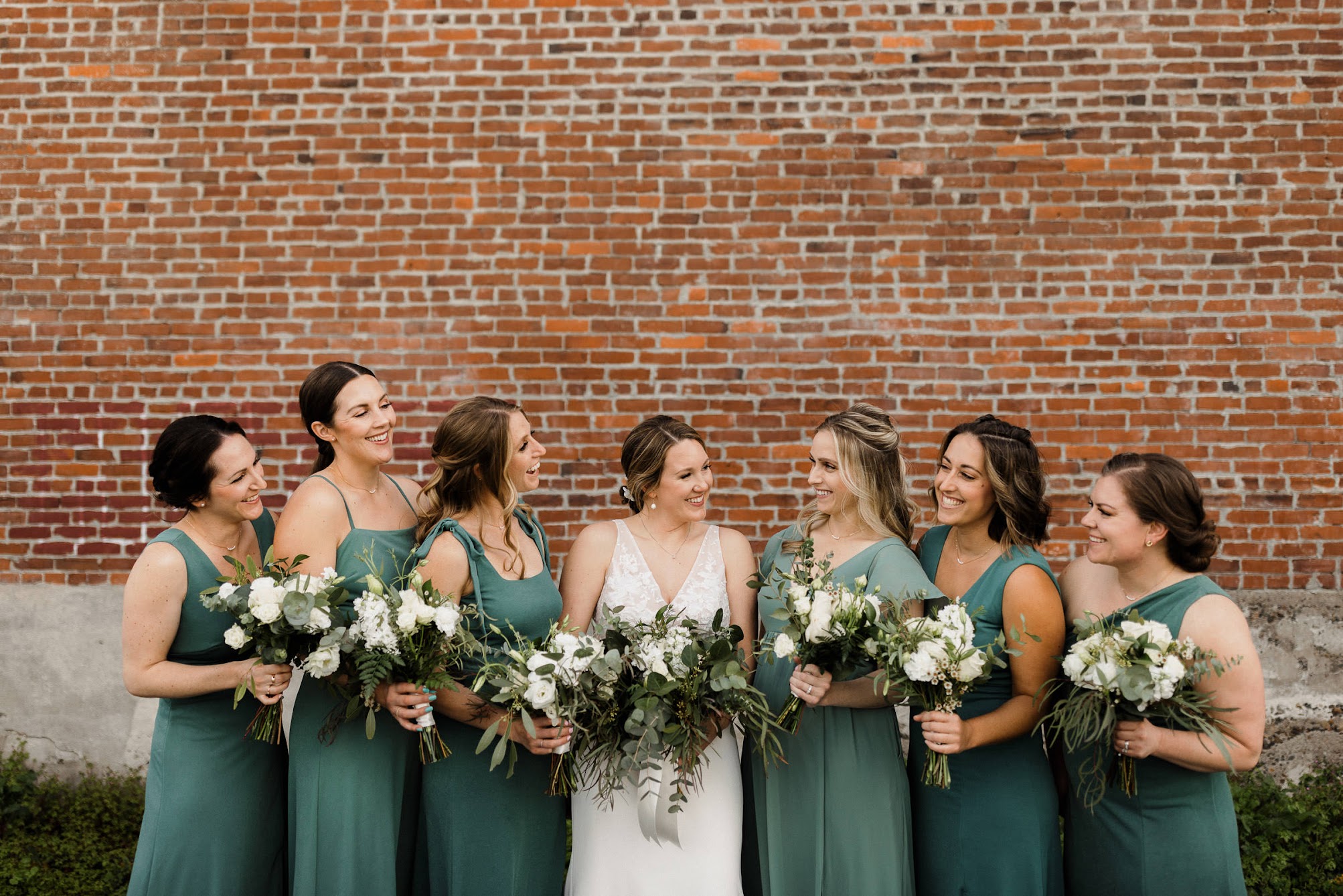 bride and her bridesmaids all looking at each other while holding their bouquets 