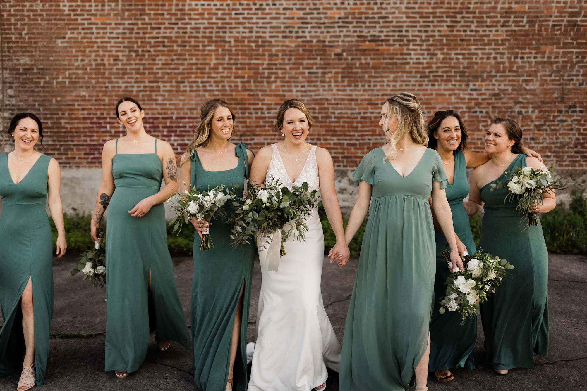 A wedding bride and her bridesmaids walking down the street, holding hands.