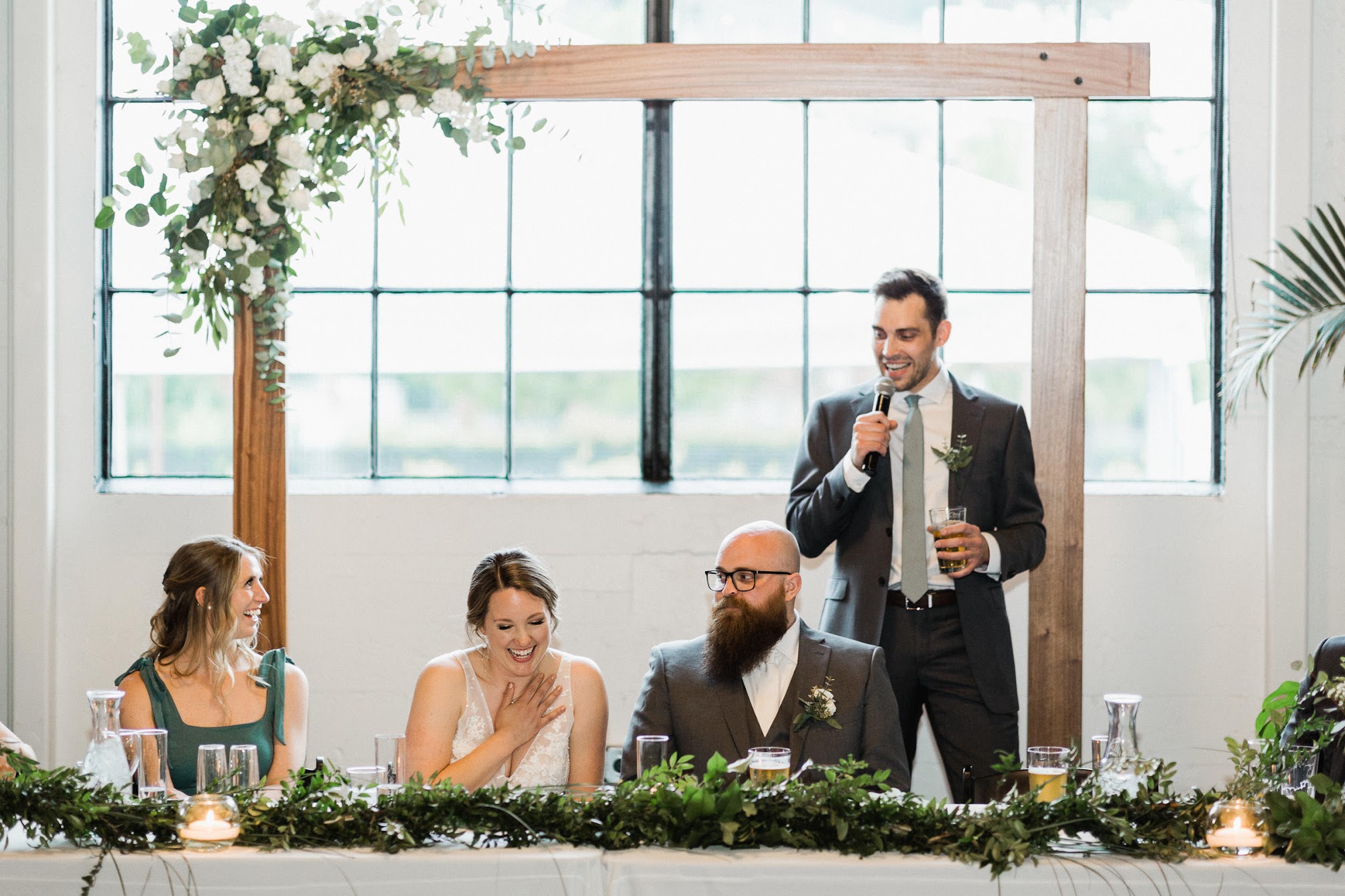 the best man standing behind the couple with a drink in his hand giving a toasts 