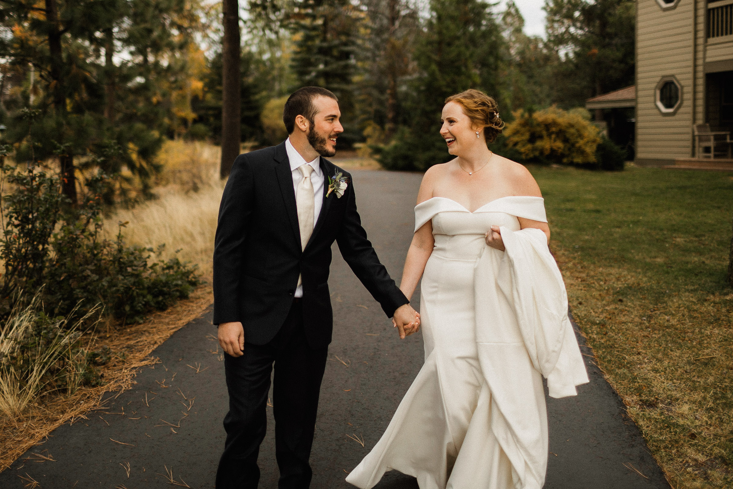 Bride and groom holds hands and smile as they walk along a path