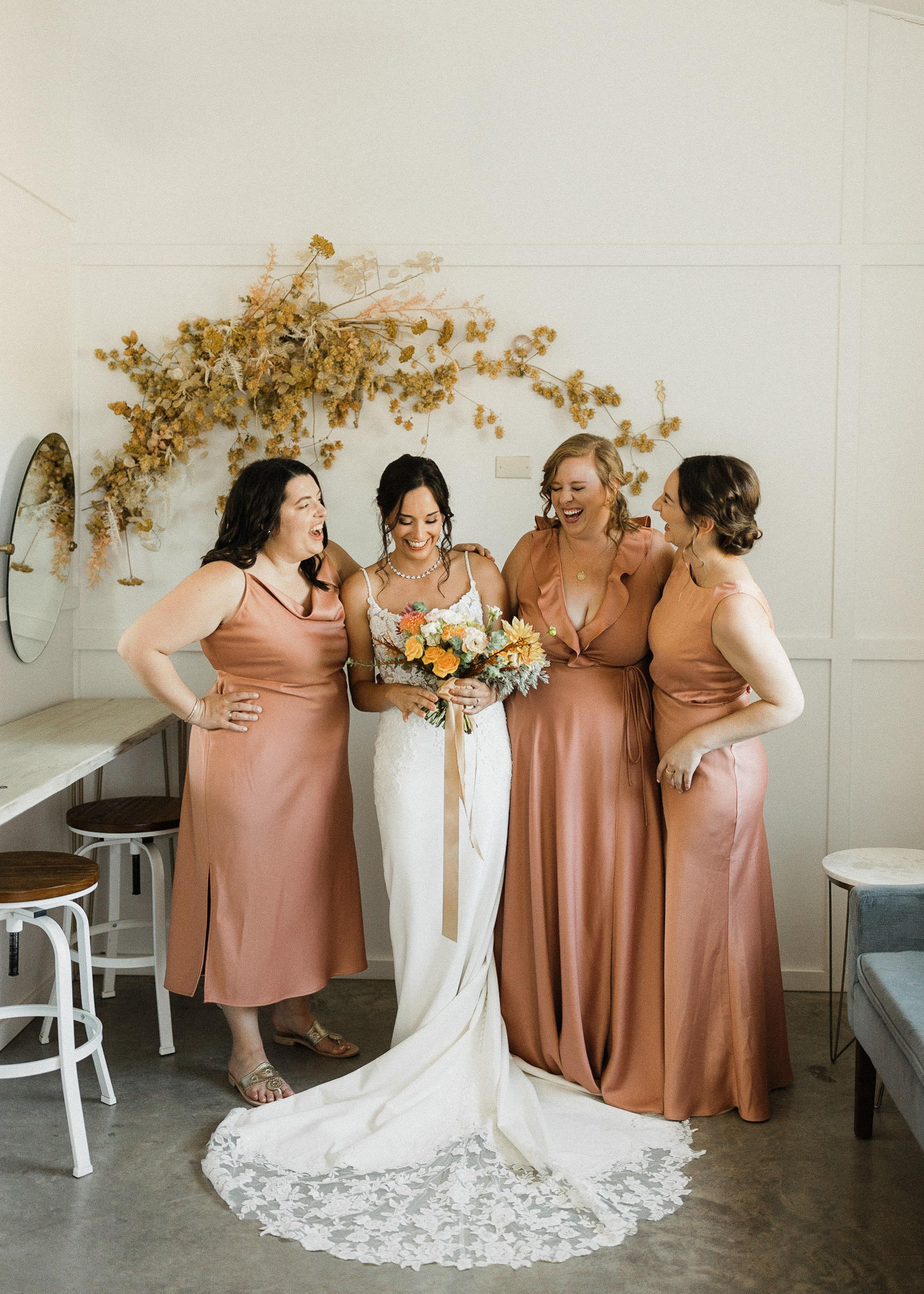 Bride and bridesmaids laugh together in a bridal suite