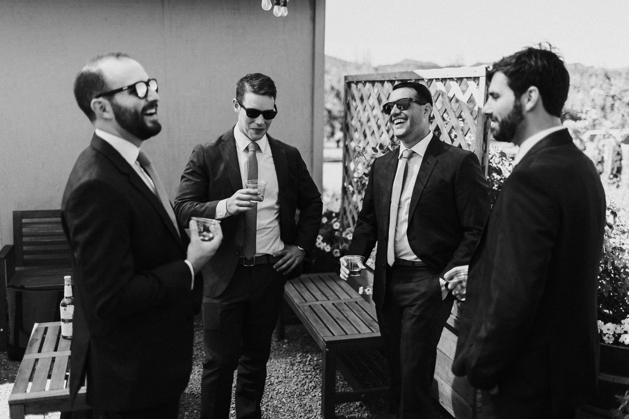 Groom and groomsmen laugh while drinking whiskey 
