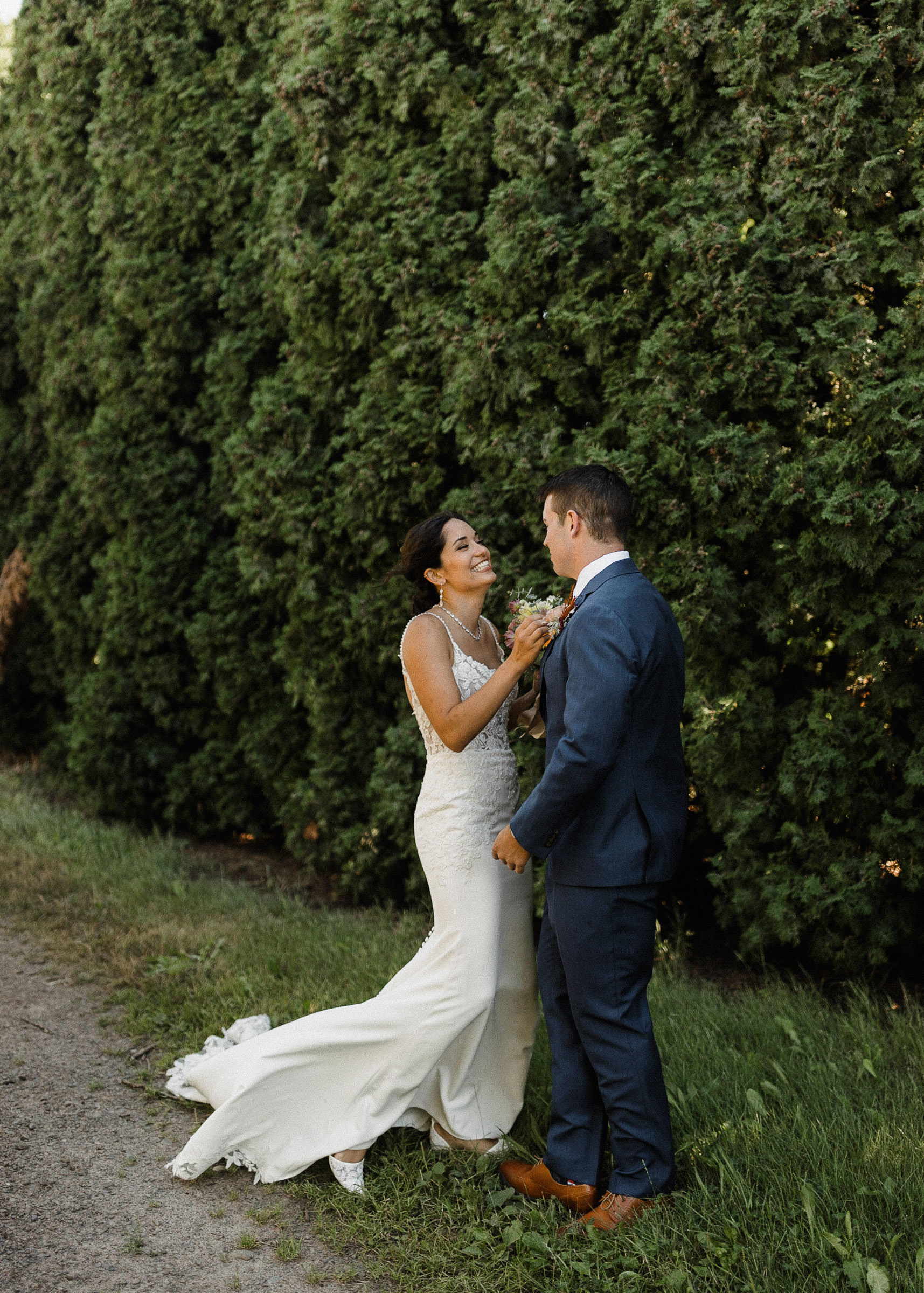 Bride smiling as she sees the groom for a first look in front of a row of hedge trees