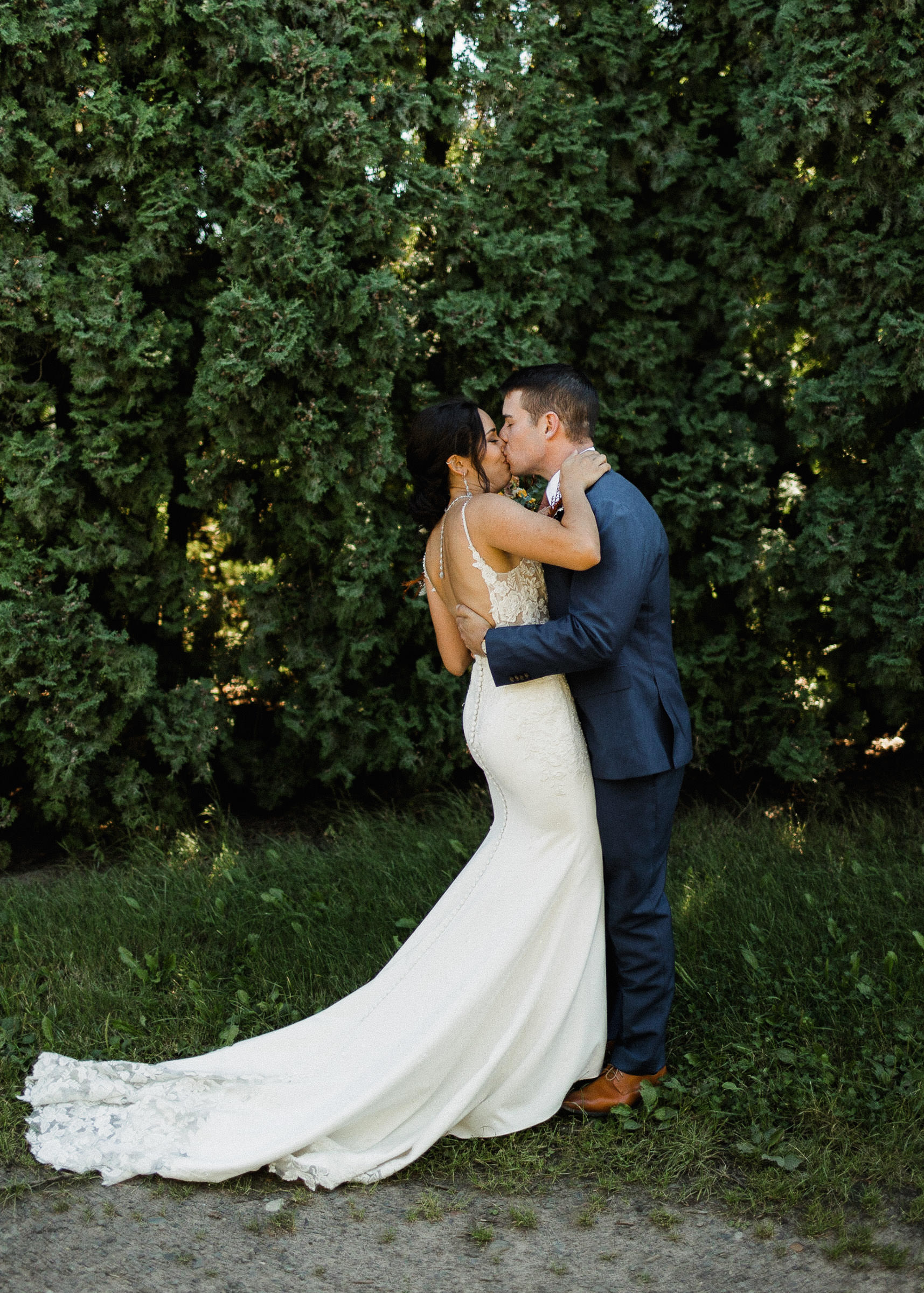 Bride and groom kiss during a first look in front of a row of hedge trees