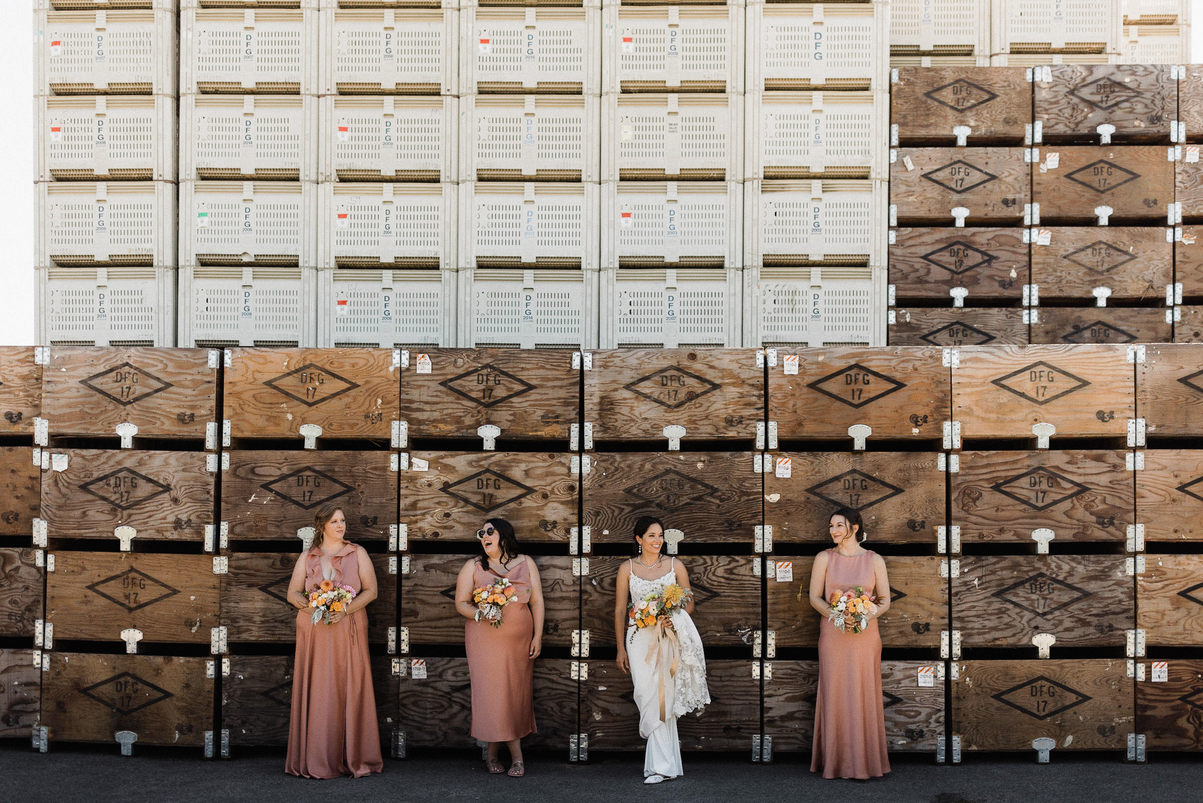 Bride and bridesmaids lined up in front of giant stack of orchard crates