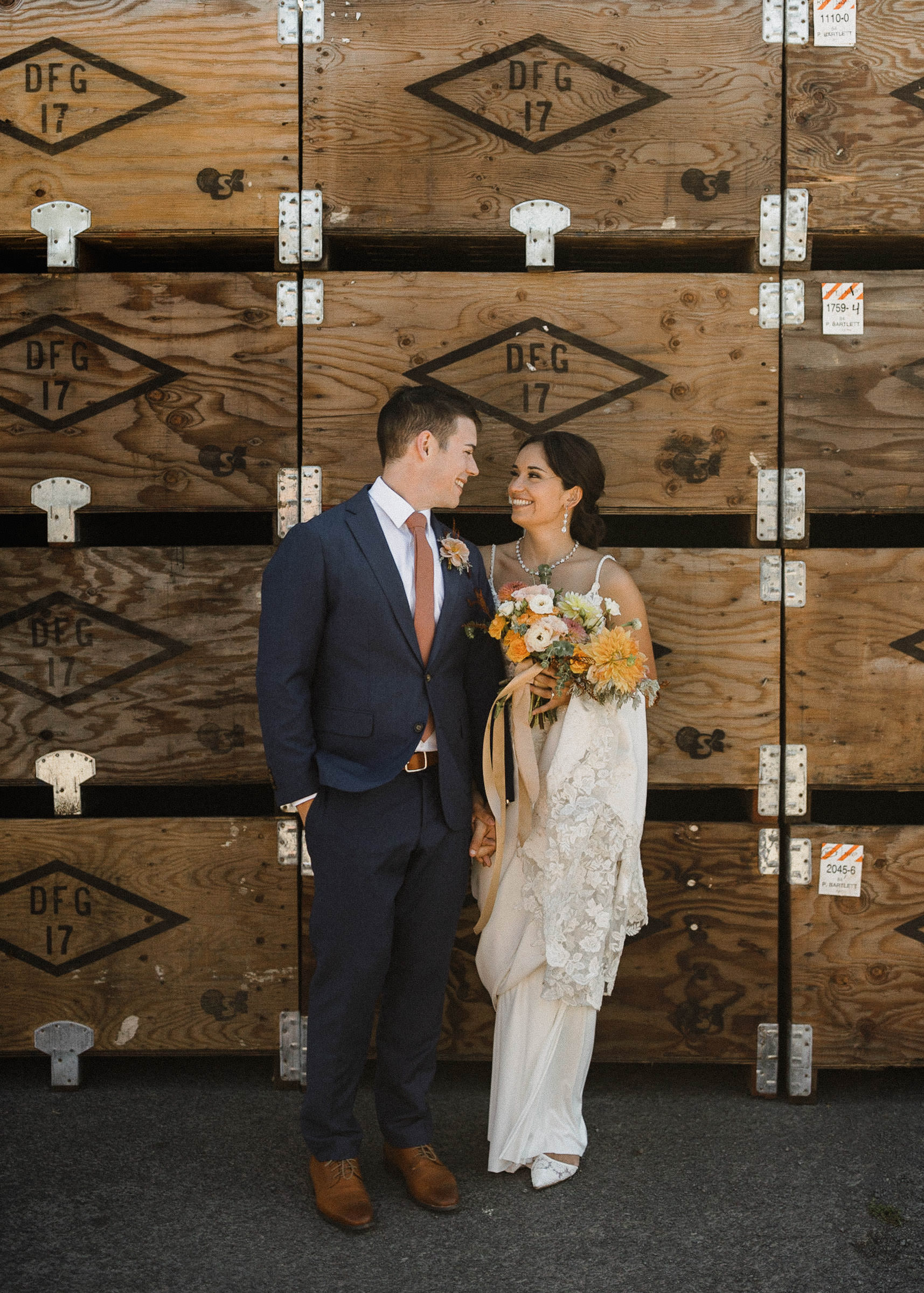 Bride and groom smiling, looking at each other in front of orchard crates