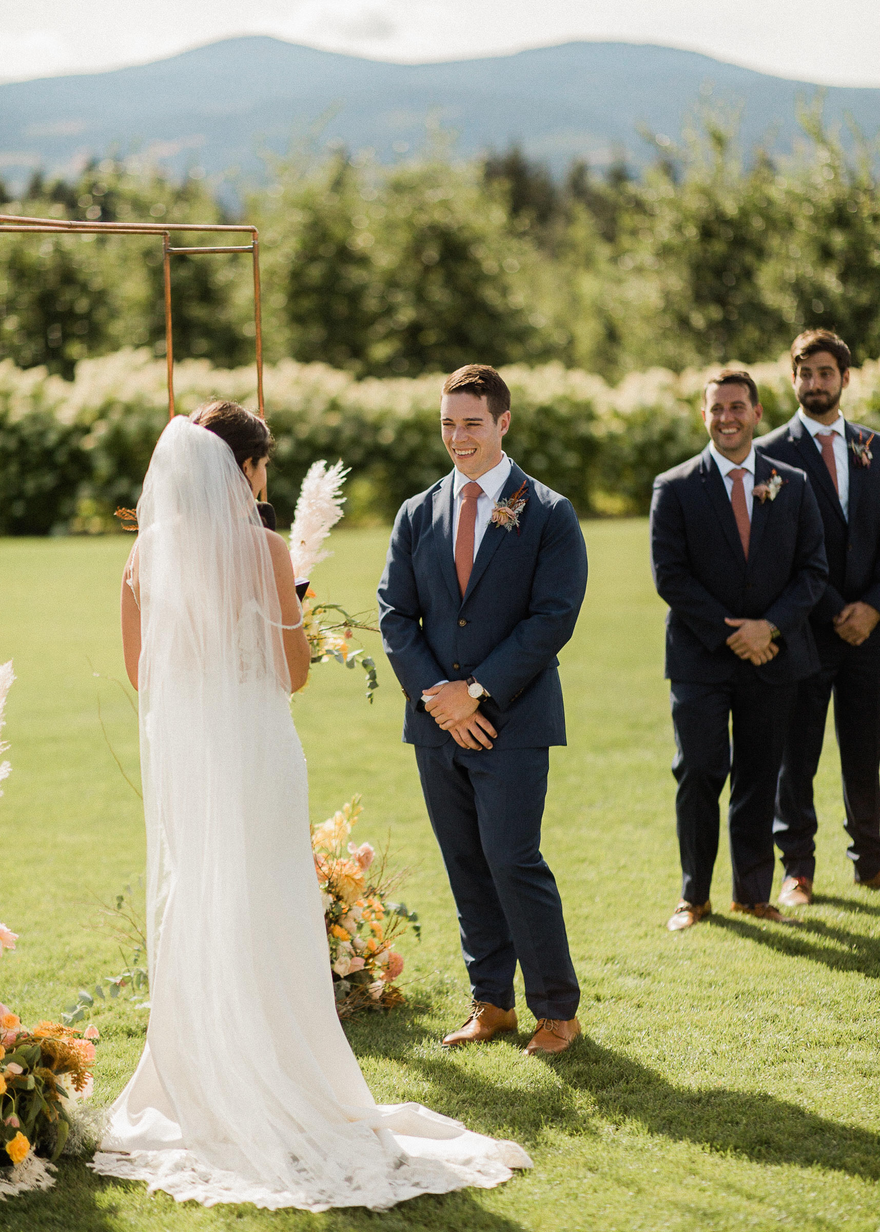 Groom smiles as bride reads vows during wedding ceremony at The Orchard
