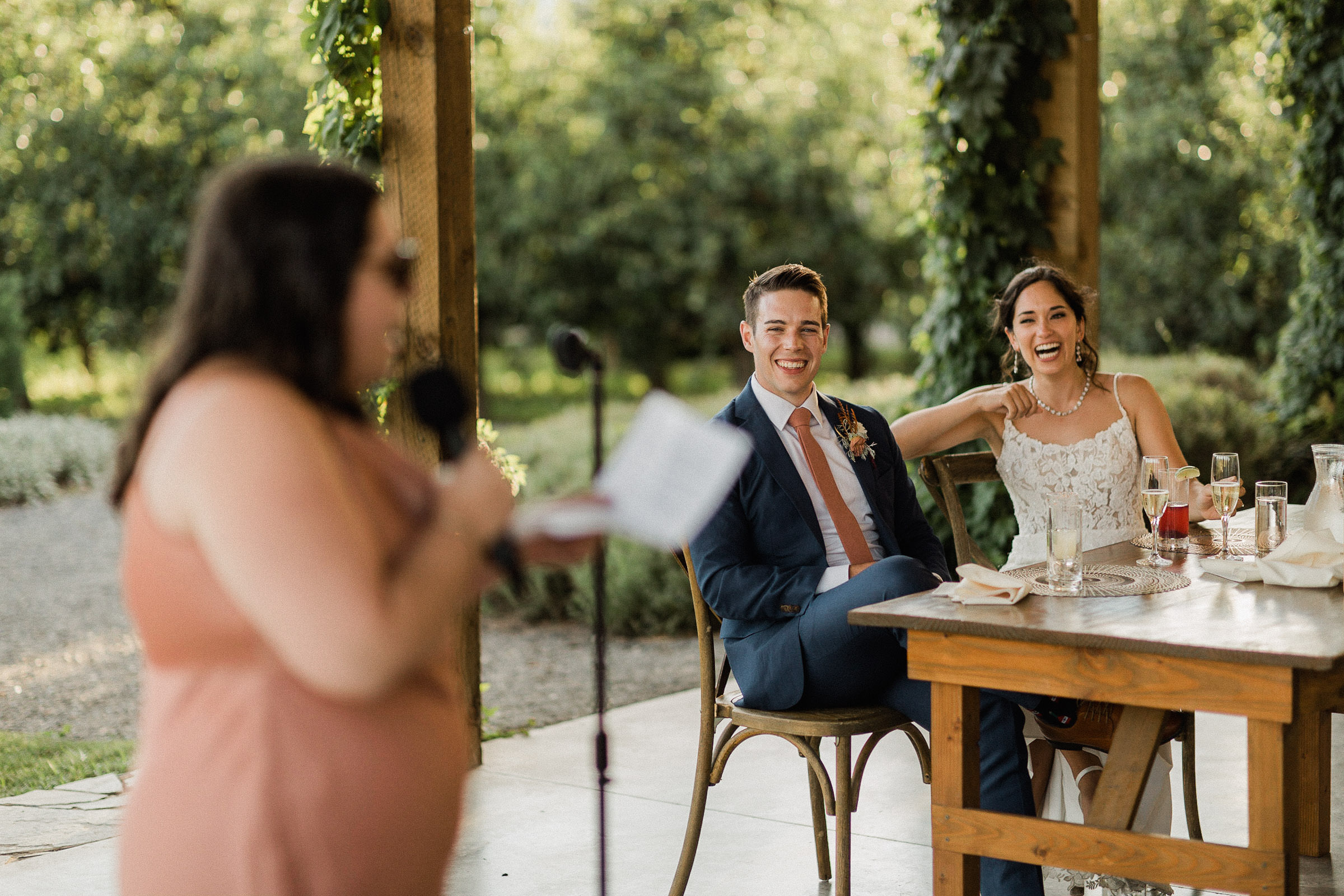 Maid of honor gives a toast as bride and groom laugh