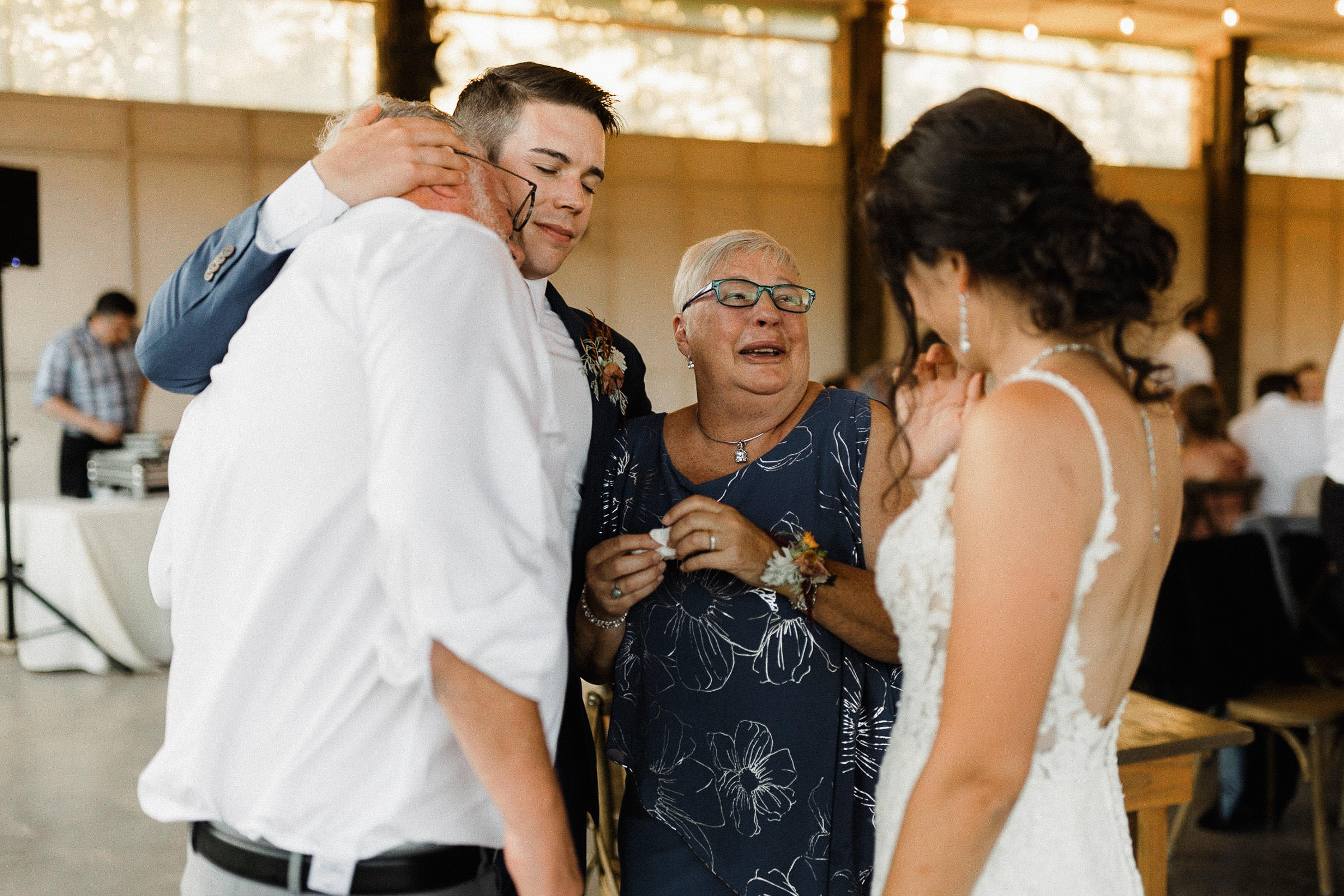 Groom, bride, and groom's parents share an emotional embrace