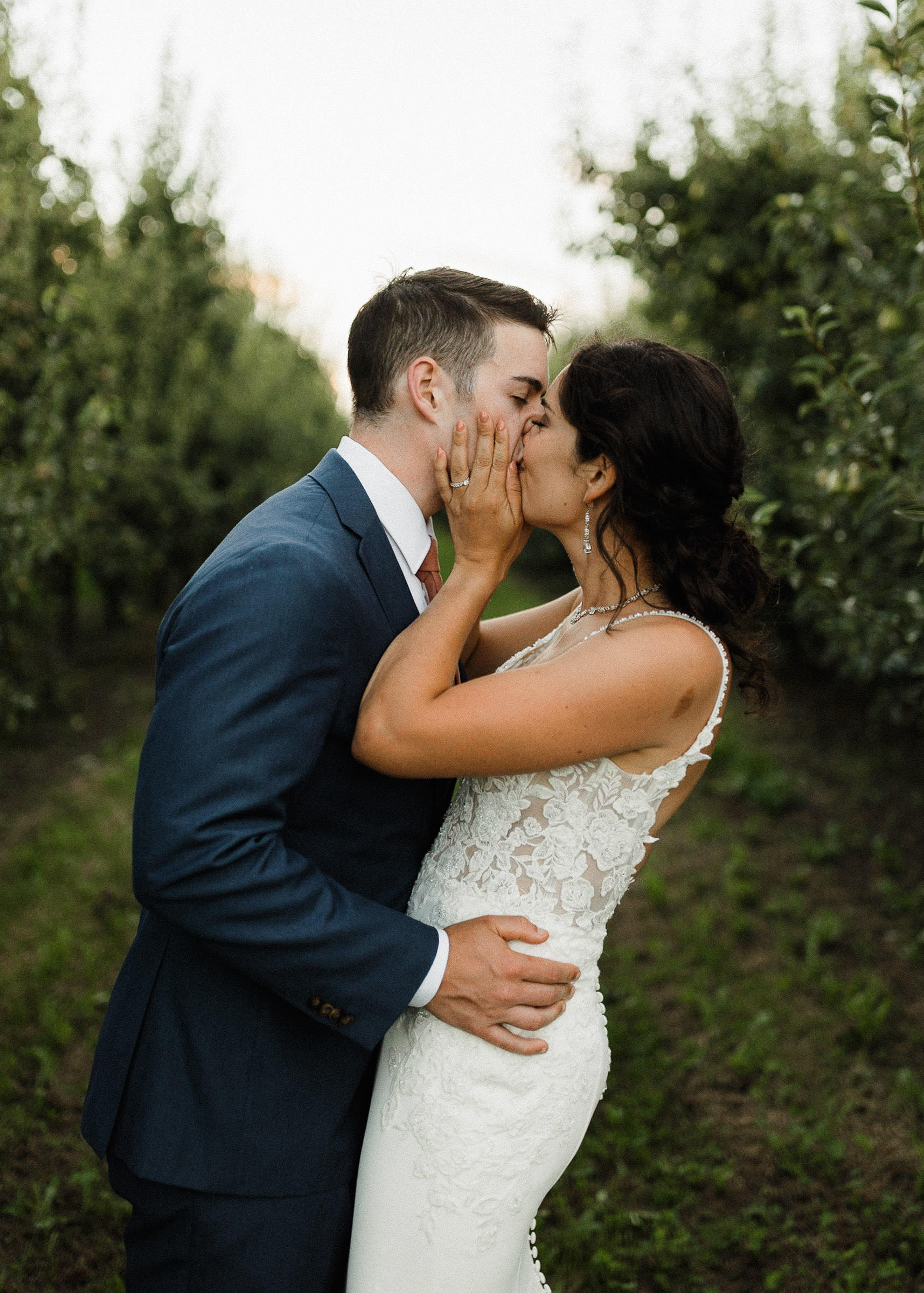 Bride and groom kiss in an orchard row