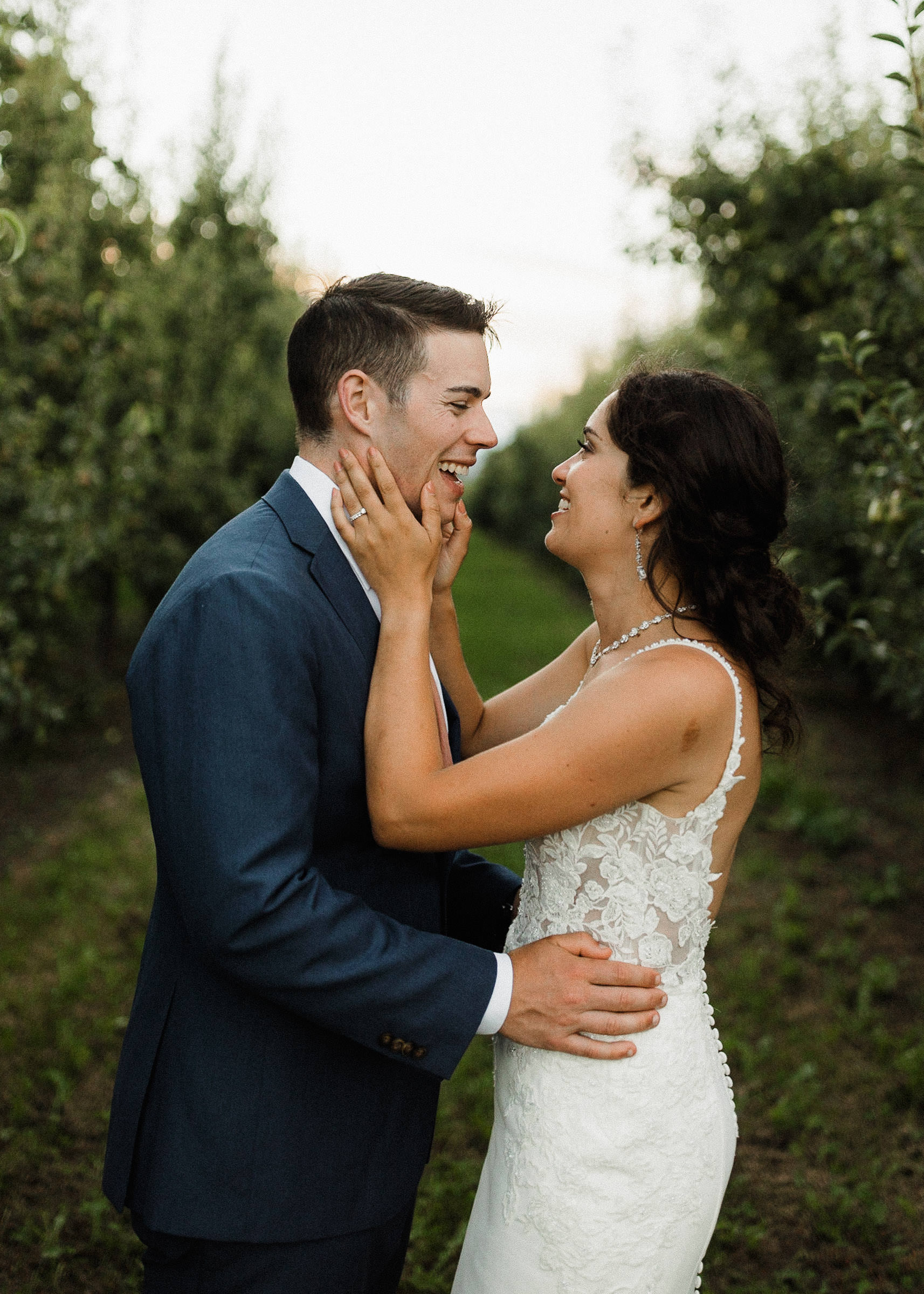 Bride holds groom's face post-kiss in an orchard row