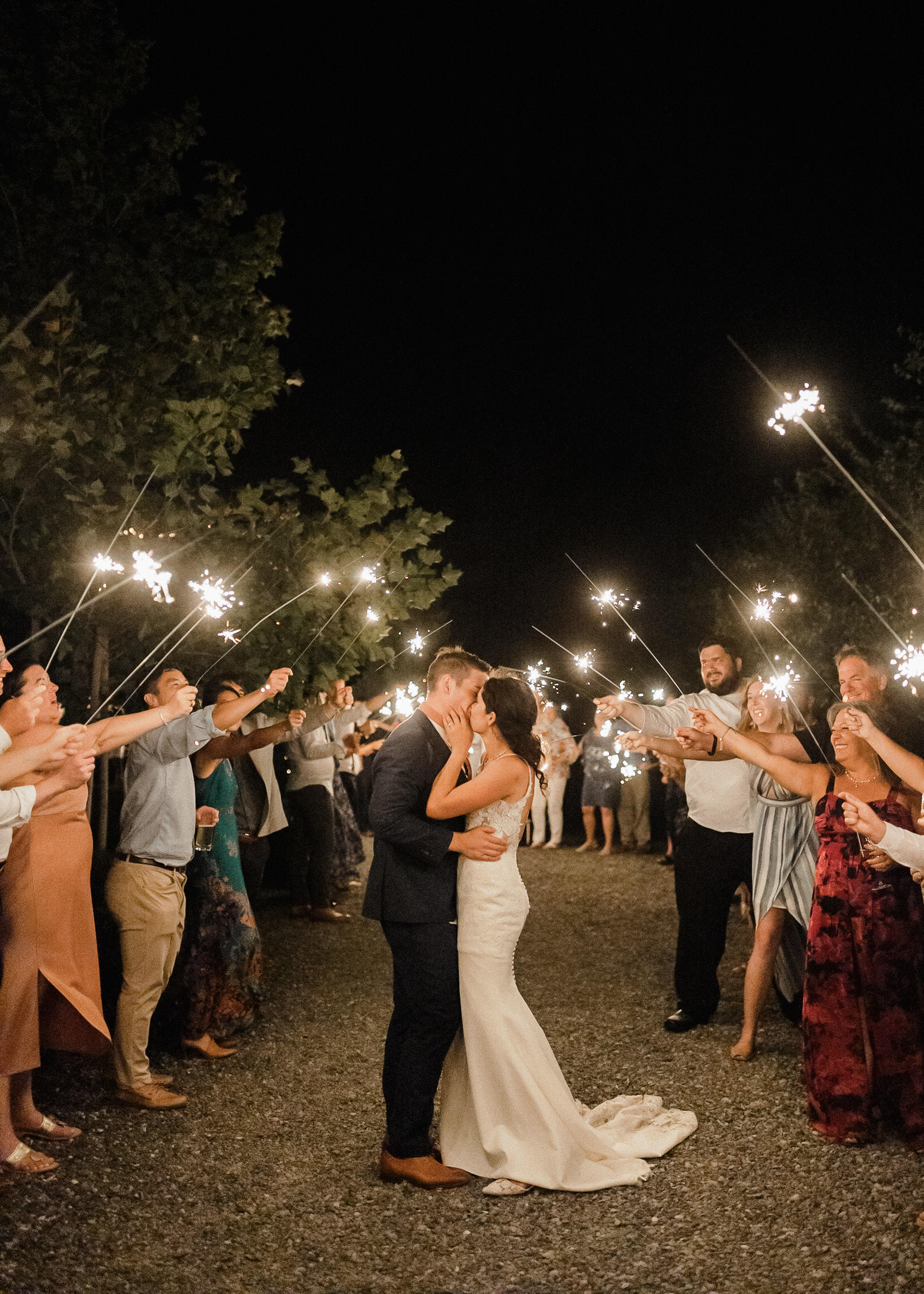 Bride and groom kiss, surrounded by guests forming a tunnel with sparklers