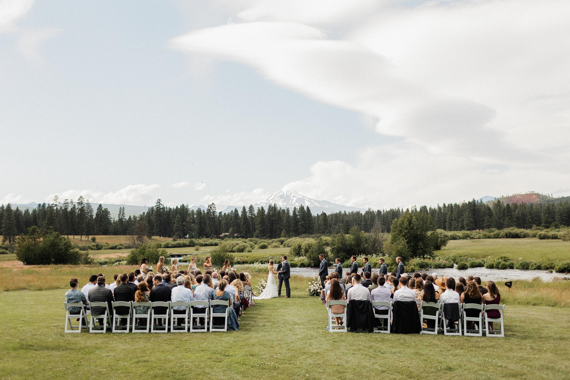 Wide view of the wedding ceremony in a field next the Metolius River, with Mt. Jefferson rising into the skyline