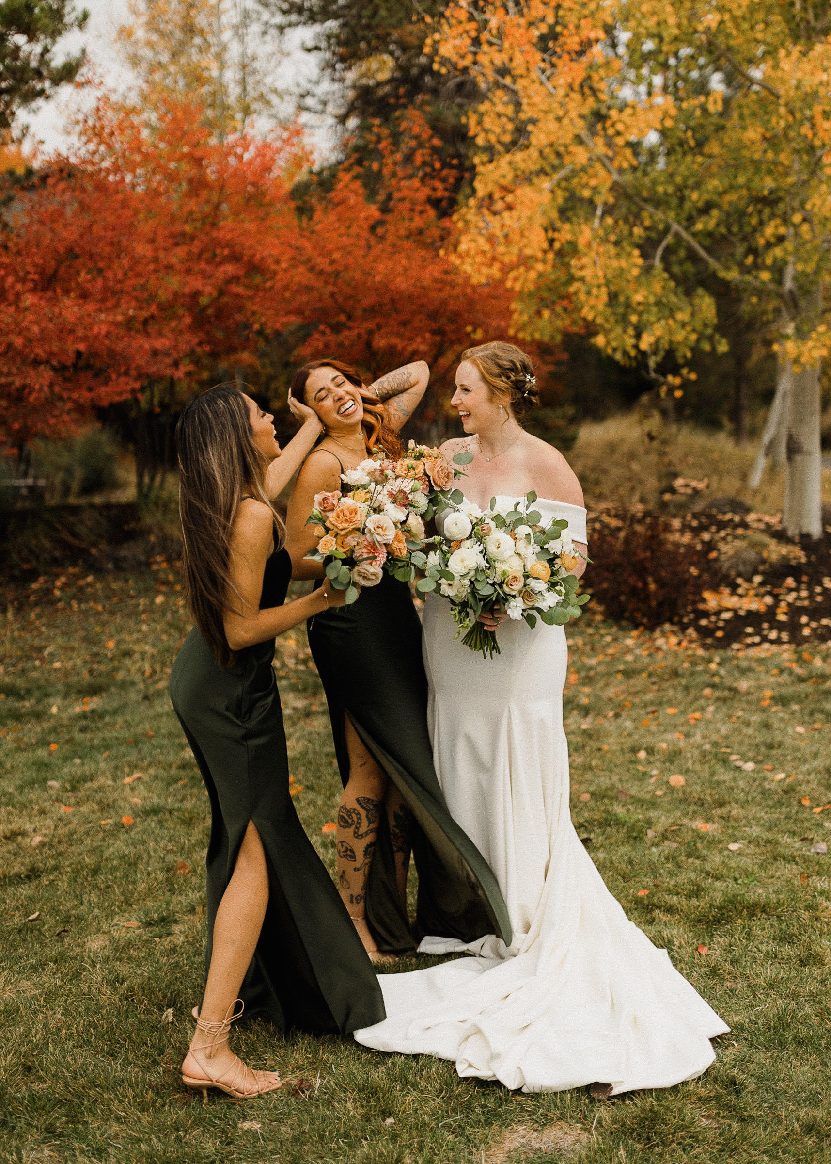 Bride and bridesmaids laugh in front of fall foliage