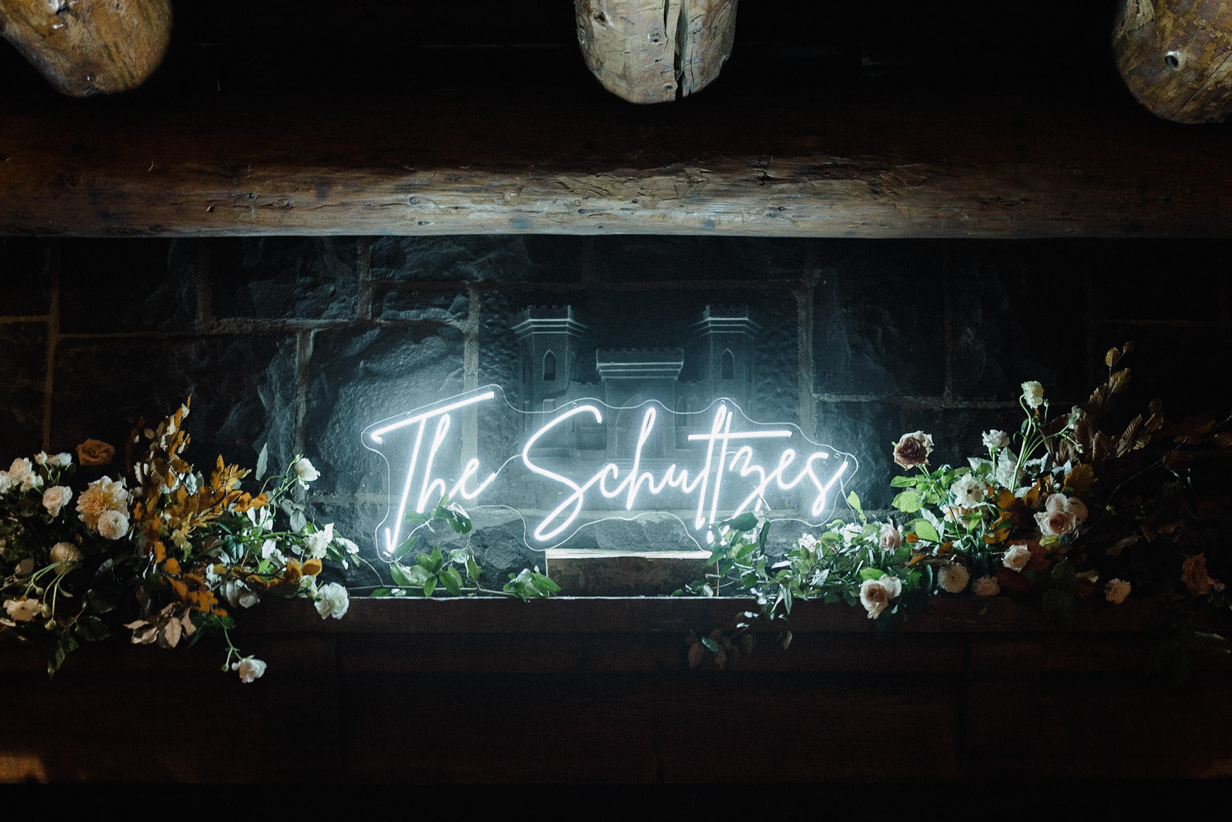 Neo sign reading "The Schultzes" sits on a mantle with floral arrangements on either side of it